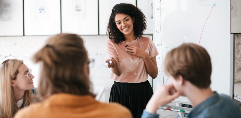 Beautiful African American lady with dark curly hair happily speaking about new project with her colleagues in office. Young smiling business woman giving presentation to coworkers